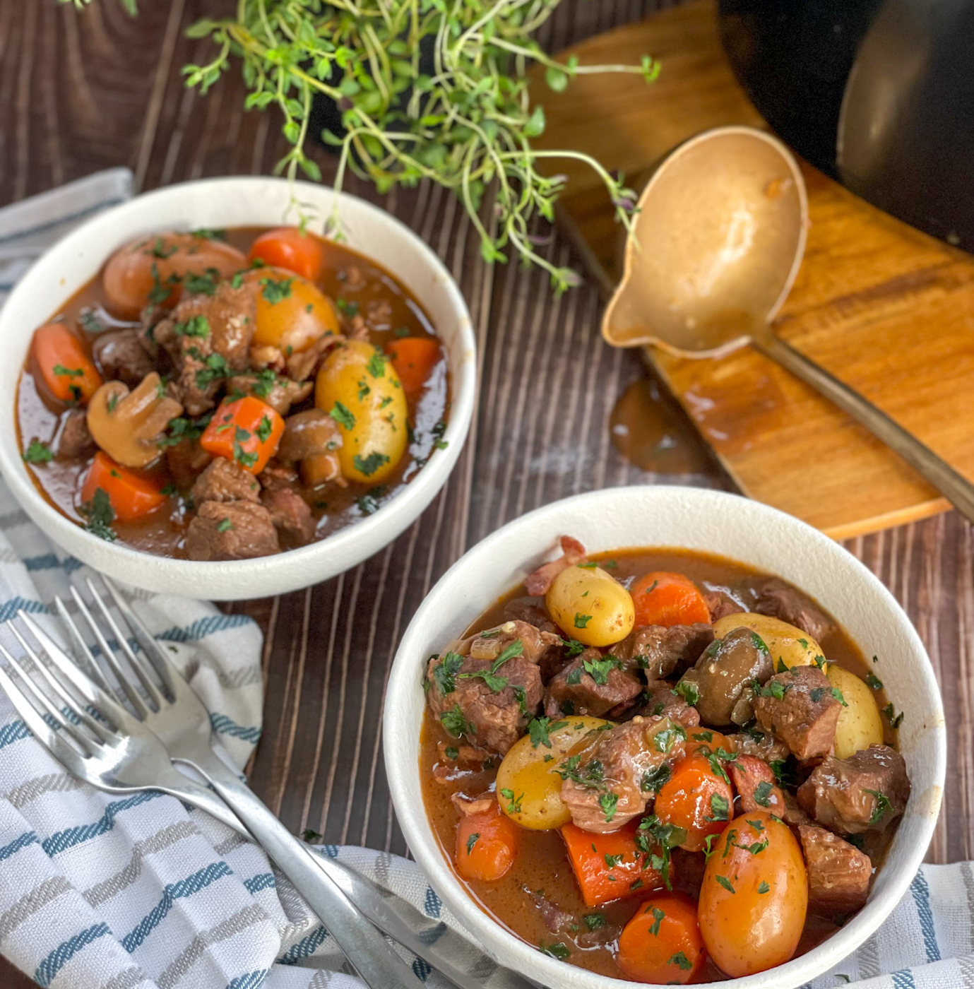 Two white bowls full of Beef Bourguignon with potatoes, mushrooms and carrots