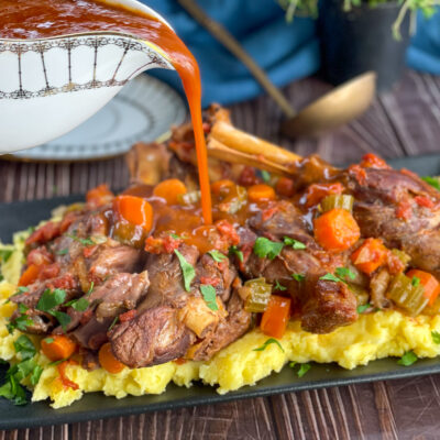 pouring thickened glossy gravy over slow cooked lamb shanks
