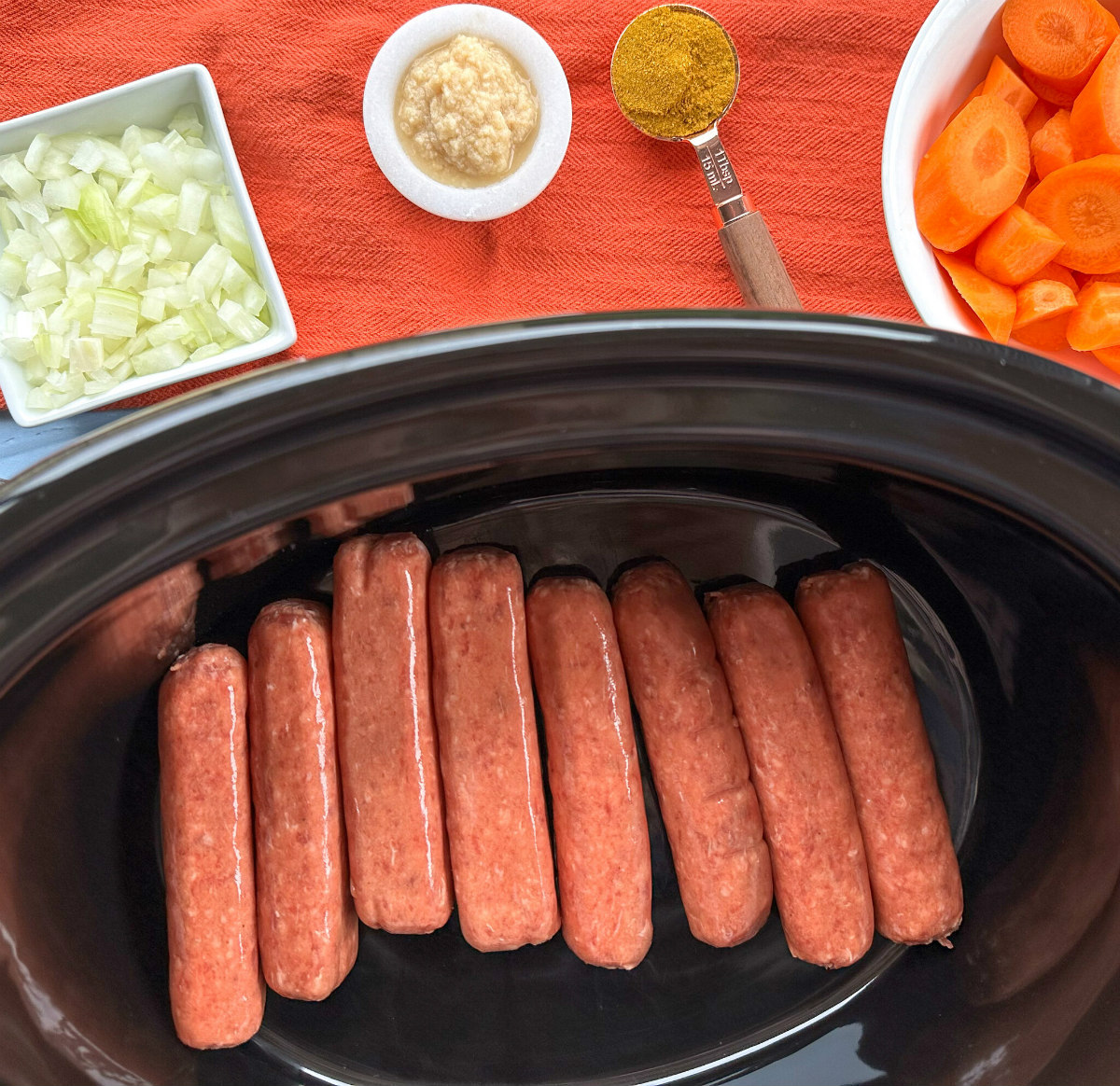 raw sausages in a slow cooker bowl with fresh vegetables ready to go in