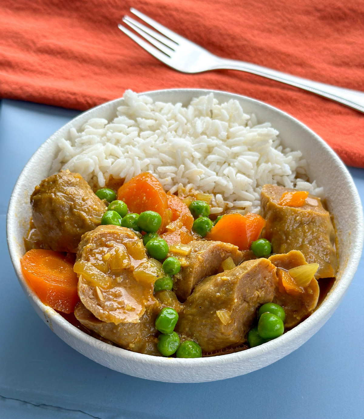 white bowl with curried sausages and rice on a blue and orange background