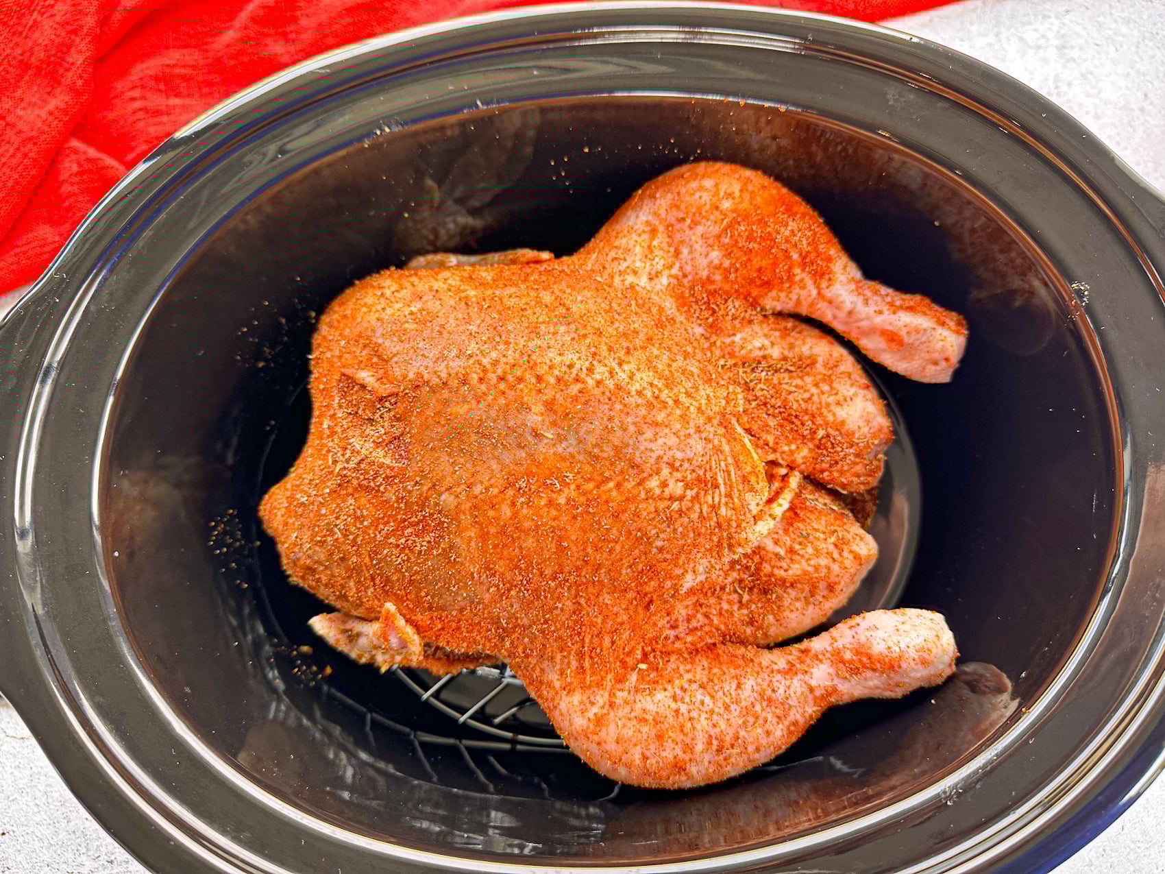 A whole raw chicken with a rub placed in a slow cooker