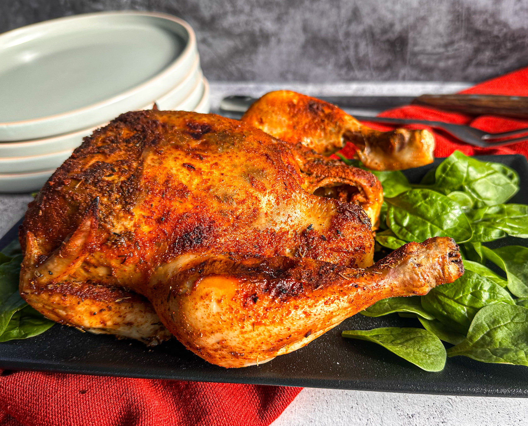 Whole Chicken slow cooked then grilled to golden brown on a black platter with spinach. 