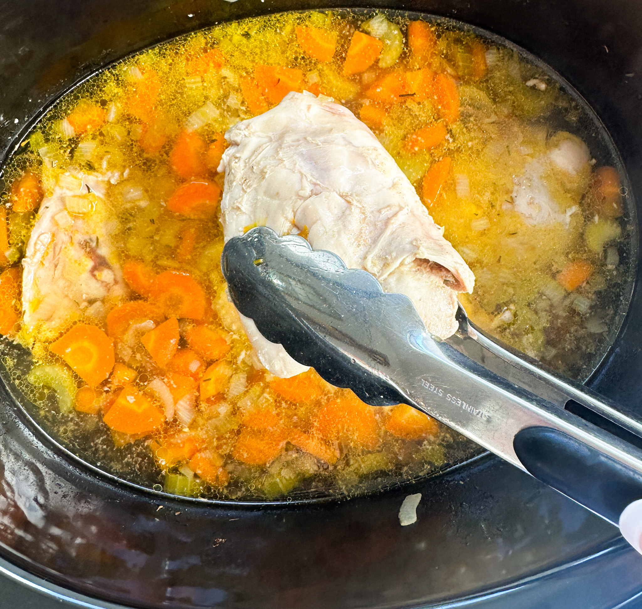 chicken thigh being removed from the slow cooker to shred