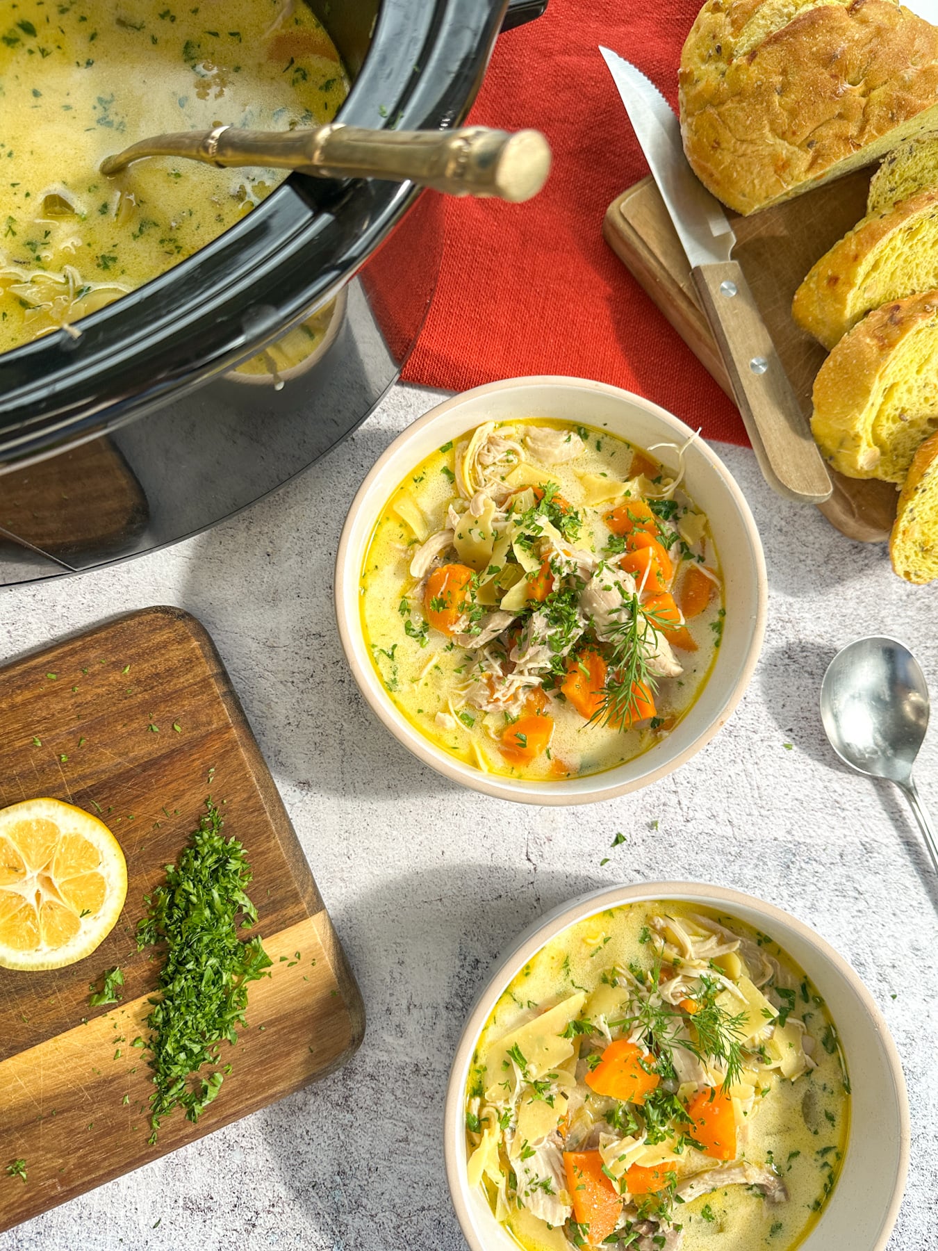 Cozy Creamy Slow Cooker Chicken Noodle Soup Slow cooker with creamy noodle soup, served in two bowls with garnishes nearby