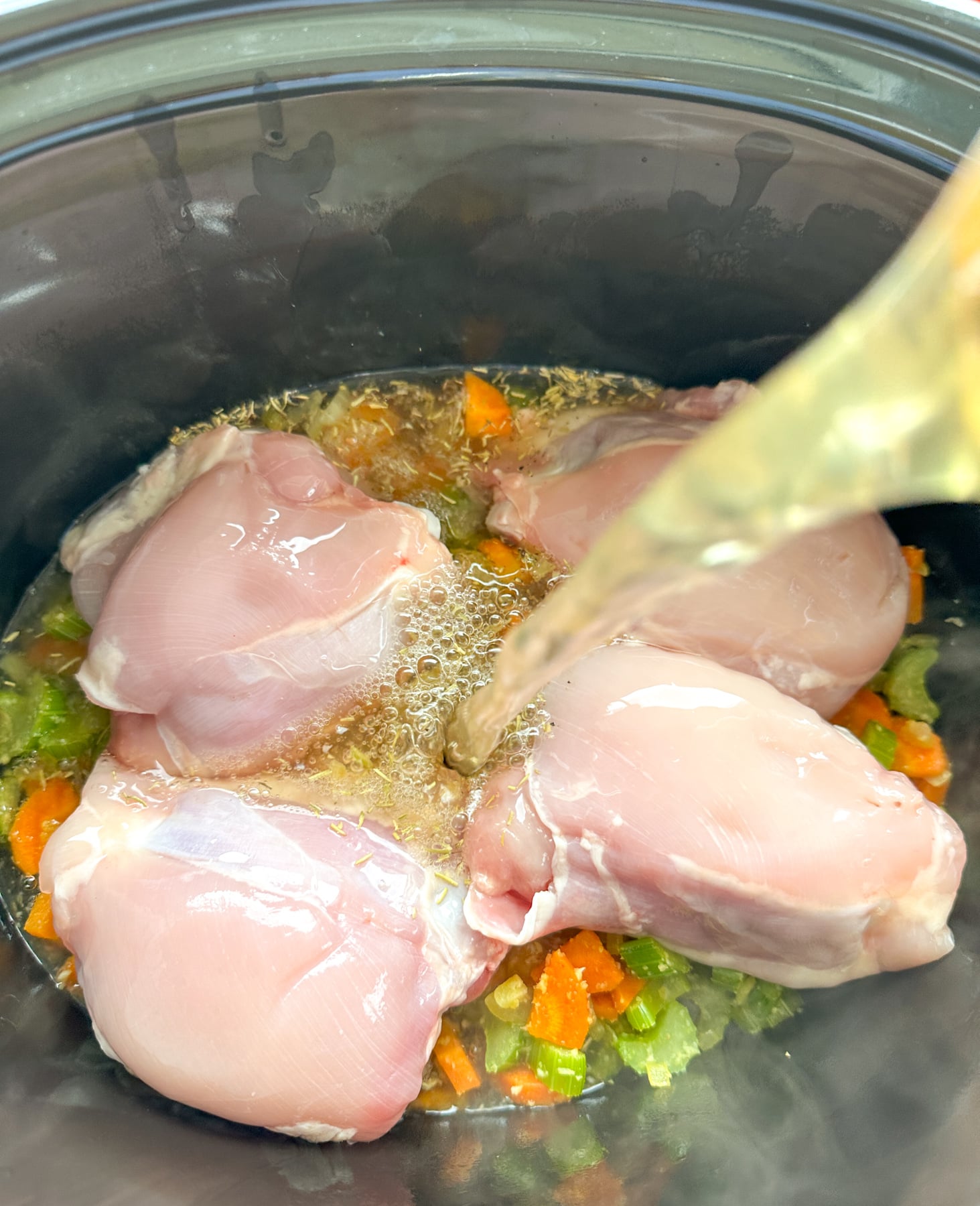 Cozy Creamy Slow Cooker Chicken Noodle Soup Pouring broth into the slow cooker for chicken noodle soup