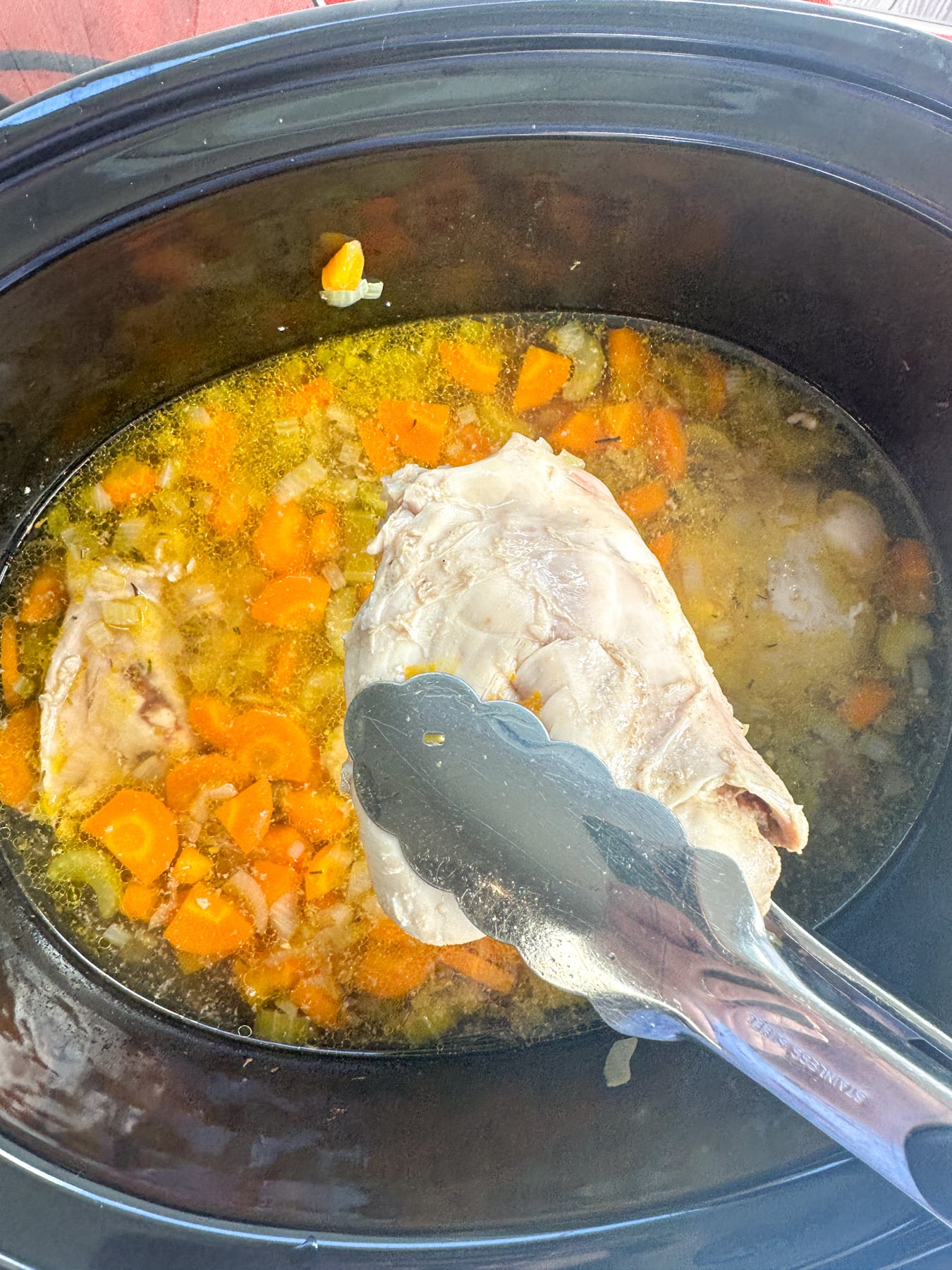 Cozy Creamy Slow Cooker Chicken Noodle Soup Cooked chicken thigh being removed from the slow cooker broth