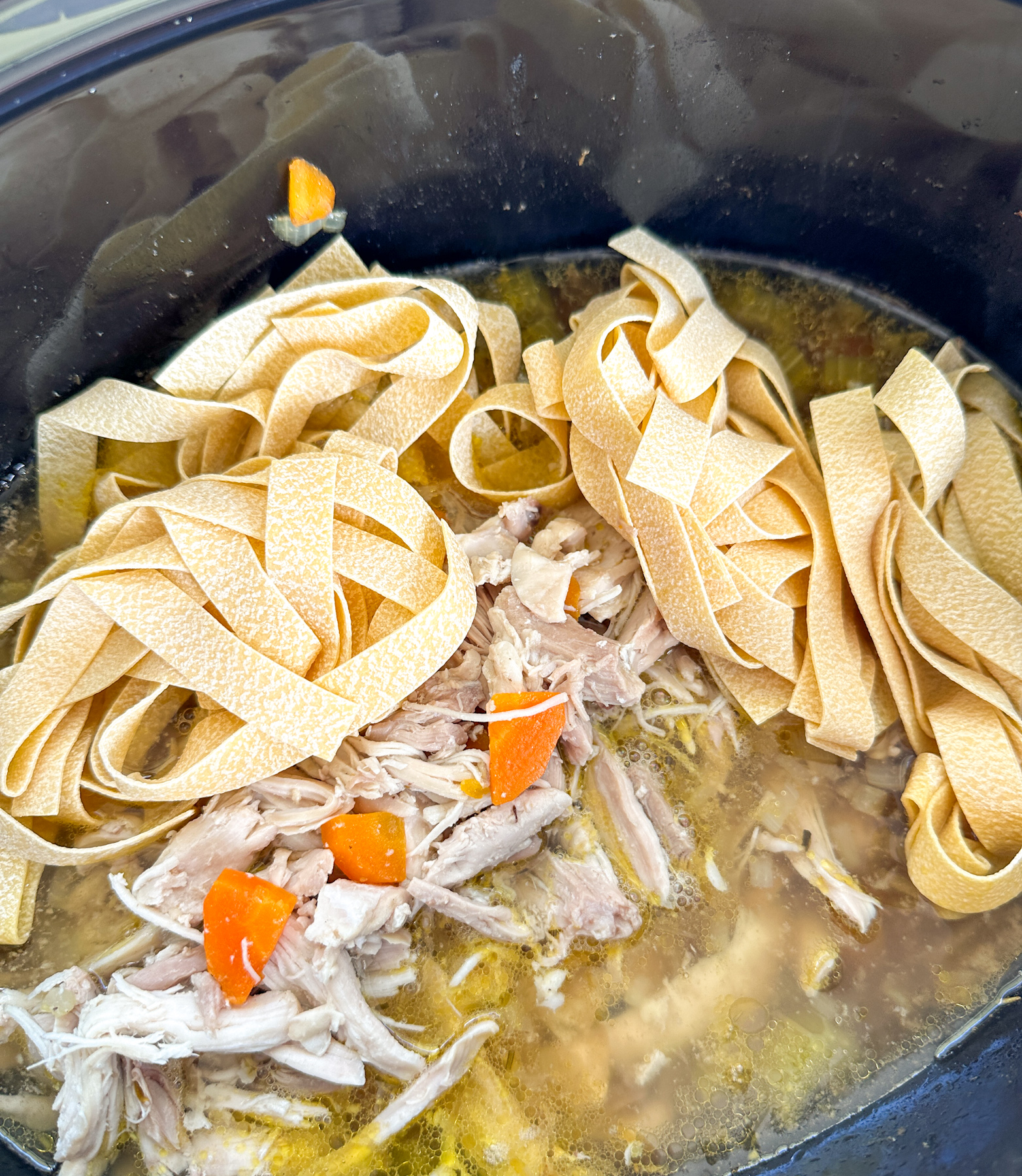 Cozy Creamy Slow Cooker Chicken Noodle Soup Shredded chicken thigh and wide egg noodles being added back into the crockpot
