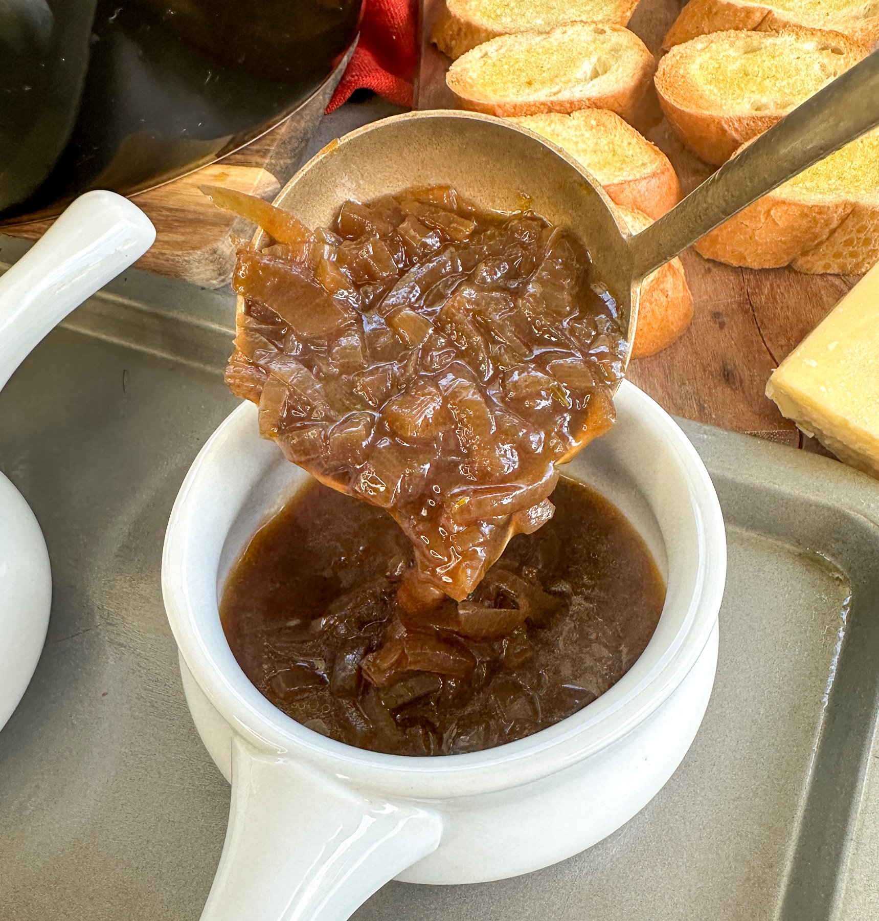 Ladling caramalized onion soup into a white French onion bowl