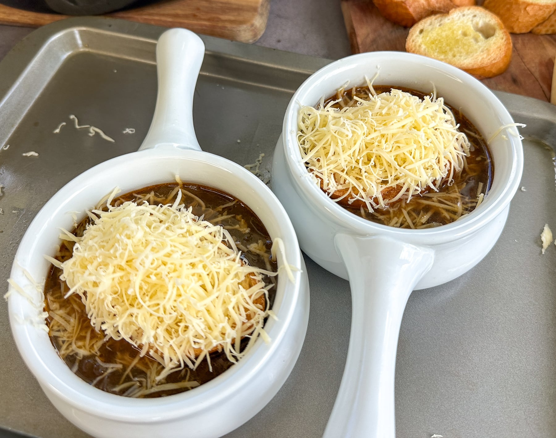 sliced baguette and grated cheese on top of French onion soup ready to melt under broiler