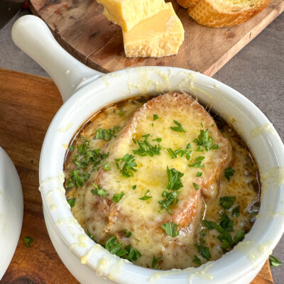 Slow Cooker French Onion soup in a white bowl with baguette and golden bubbling cheese melted on the top and fresh parsley