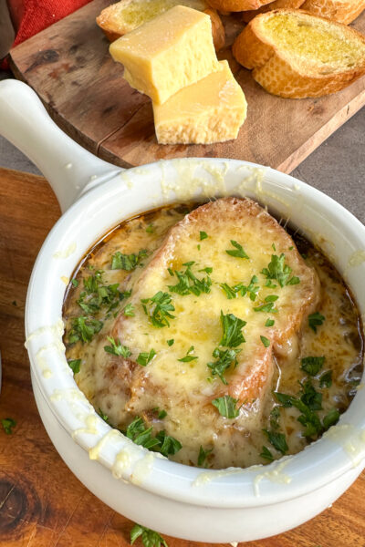 Slow Cooker French Onion soup in a white bowl with baguette and golden bubbling cheese melted on the top and fresh parsley