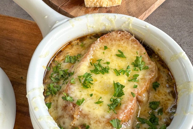 Slow Cooker French Onion soup in a white bowl with baguette and golden bubbling cheese melted on the top and fresh parsley
