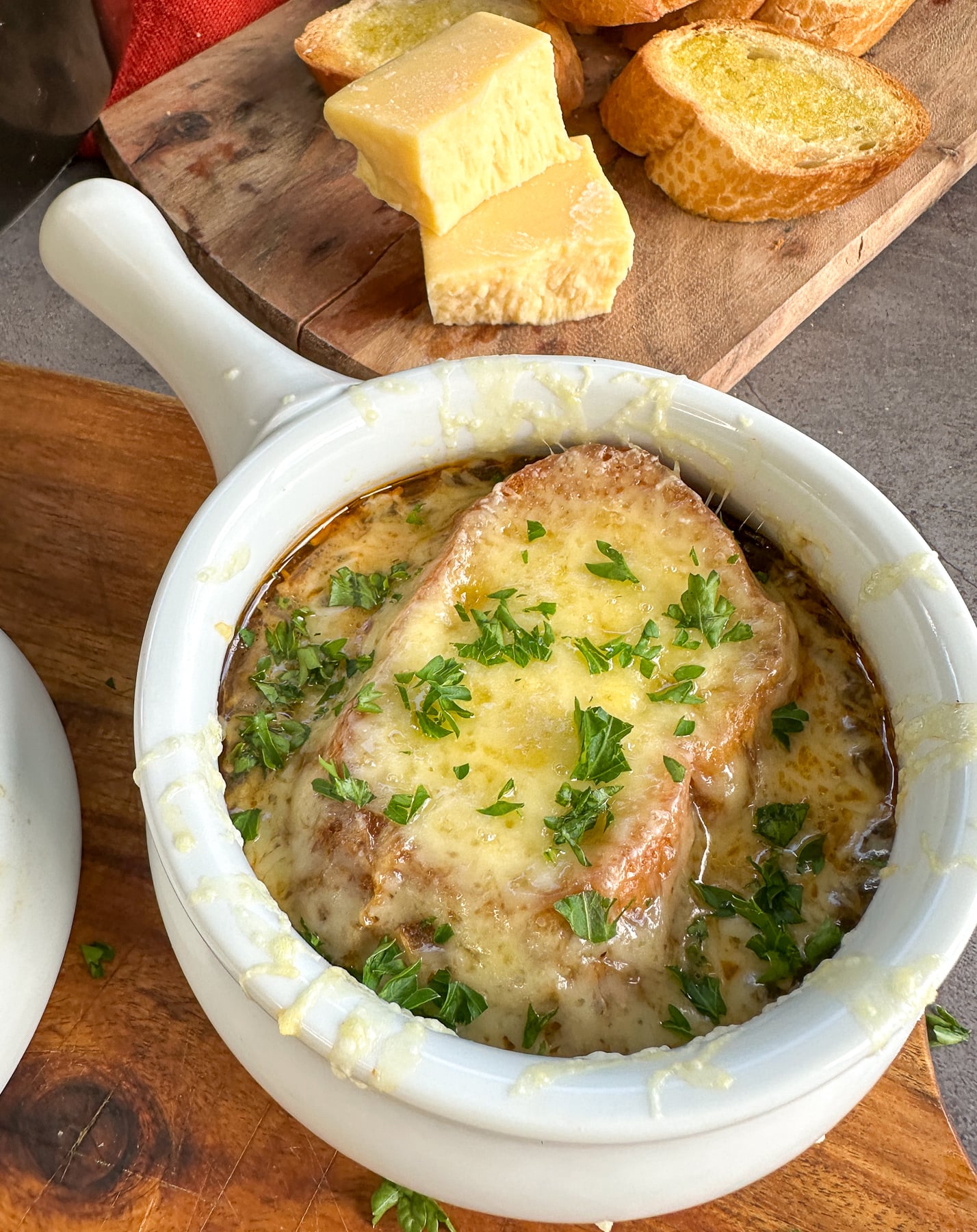 Bowl of French onion soup with bread and melted cheese sprinkled with fresh parsley
