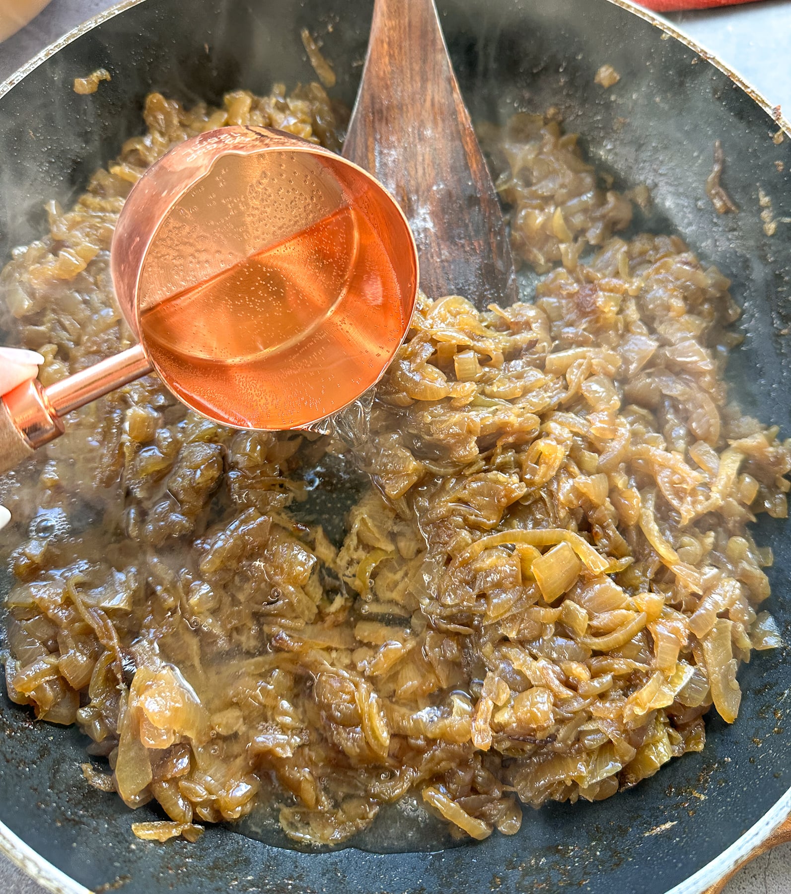 Pouring white wine into caramelized onions in a pan