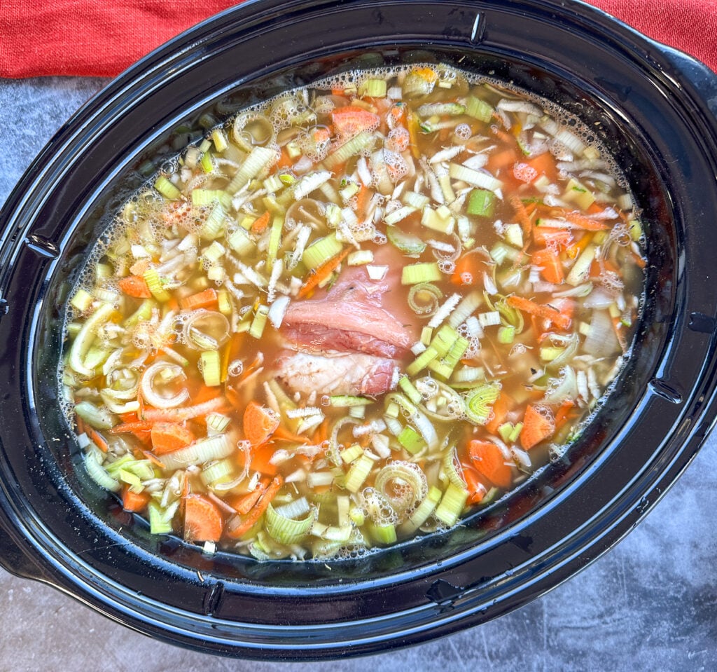 slow cooker filled with vegetable soup ingredients and ham hock