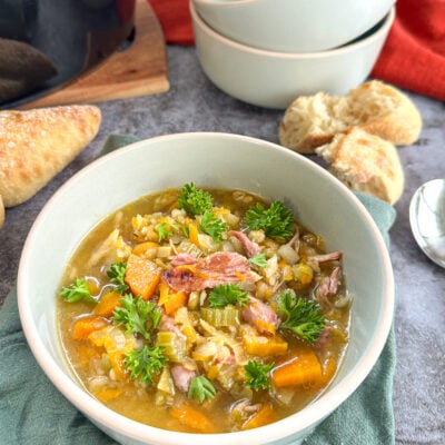 Bowl of slow cooker ham and vegetable soup with split peas and crusty bread