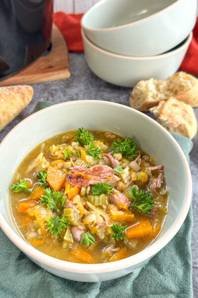 Bowl of slow cooker ham and vegetable soup with split peas and crusty bread