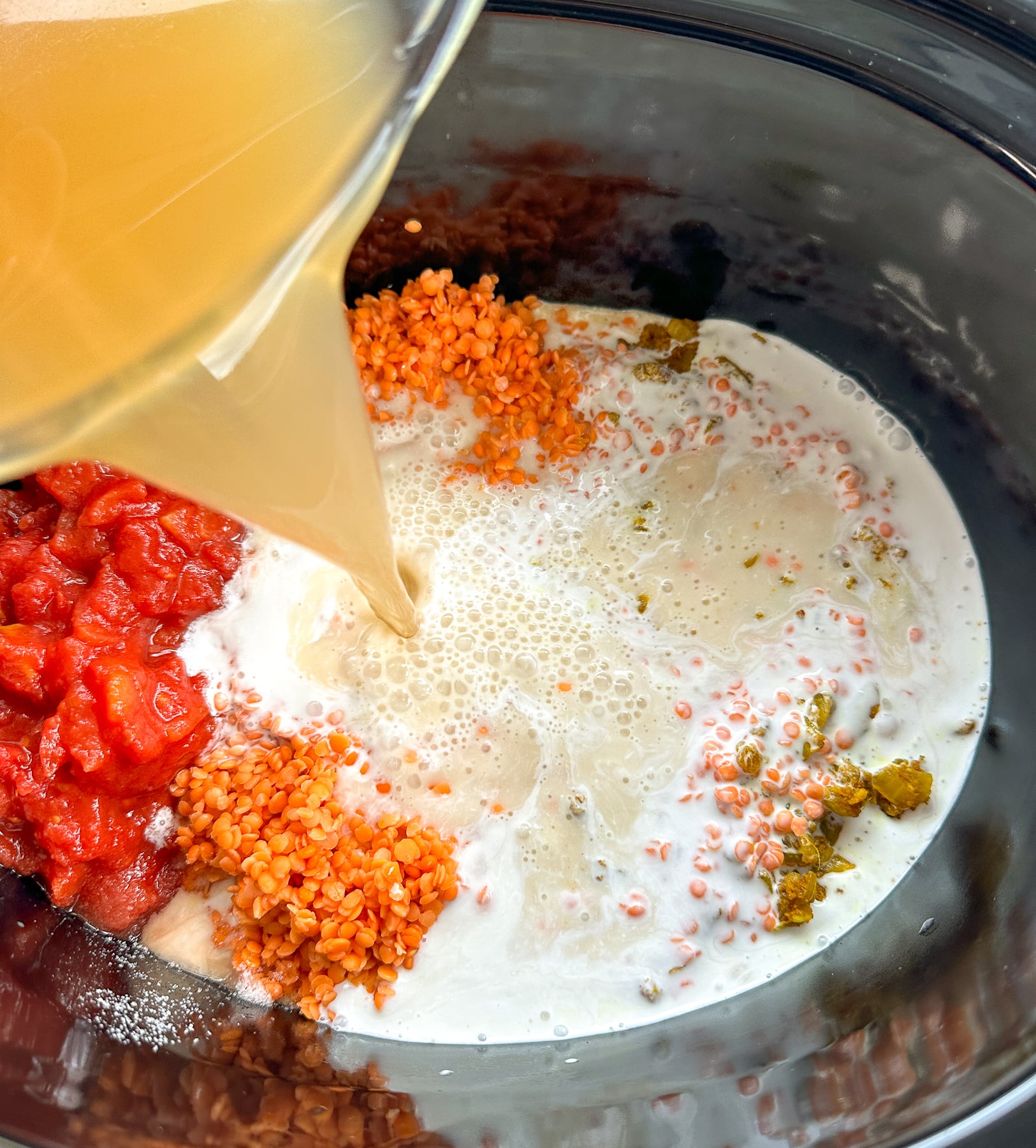 pouring broth into the slow cooker for the red lentil curry