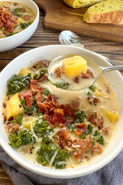 Zuppa Toscana with generous toppings of bacon and parsley being spooned from the bowl with potato, sausage and kale on the spoon