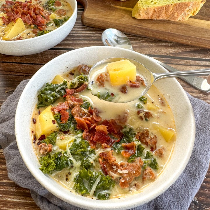 Zuppa Toscana with generous toppings of bacon and parsley being spooned from the bowl with potato, sausage and kale on the spoon