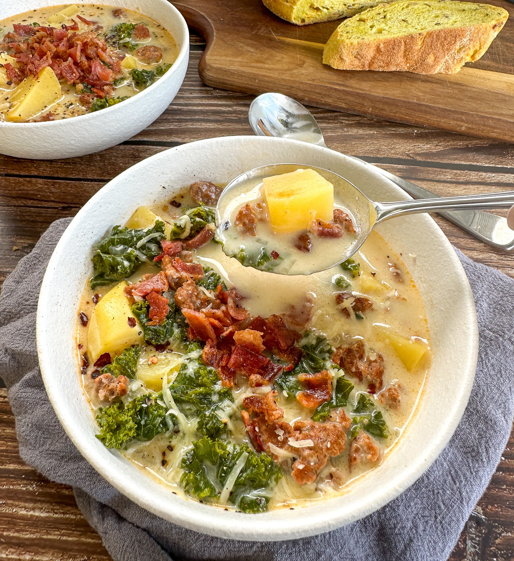 Zuppa Toscana with generous toppings of bacon and parsley being spooned from the bowl with potato, sausage and kale on the spoon