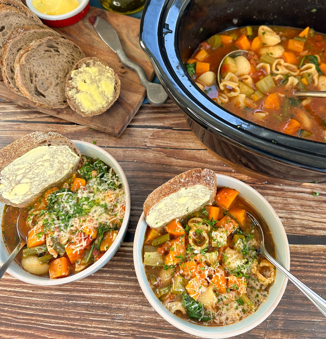 two bowls of hearty minestrone soup and the slow cooker filled with warm soup and a side of bread