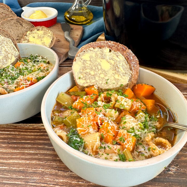 bowl of slow cooker minestrone soup with fresh vegetables, pasta and sliced bread to serve