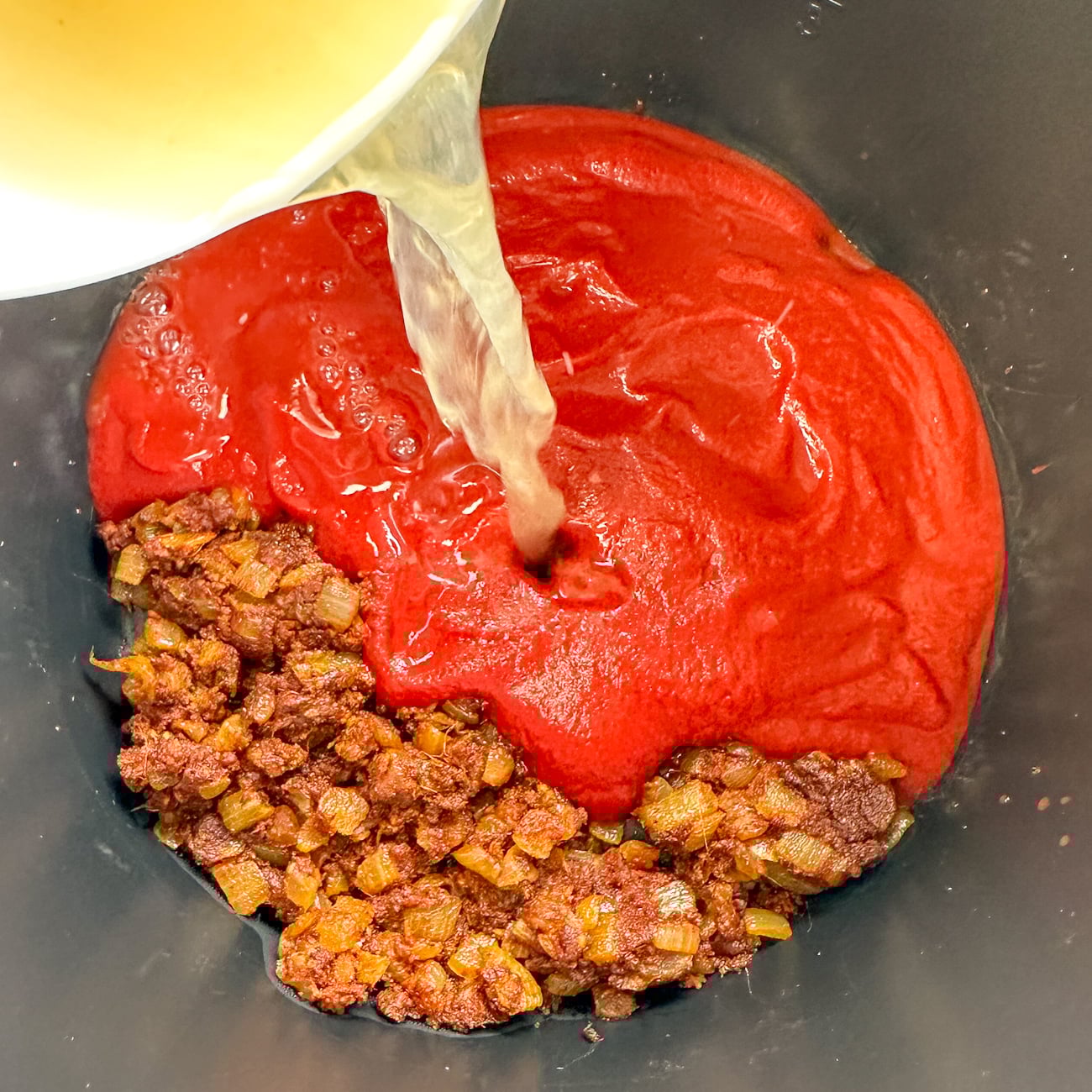 adding the liquids to the butter chicken in the slow cooker