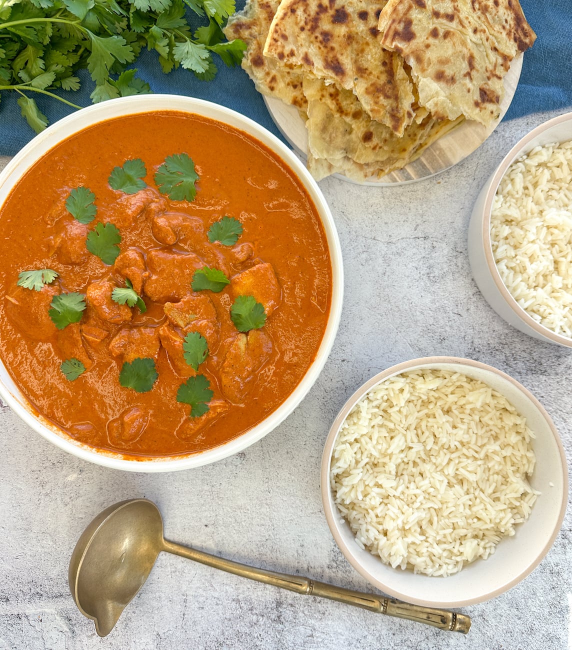 Bowl of butter chicken with bowls of rice for serving