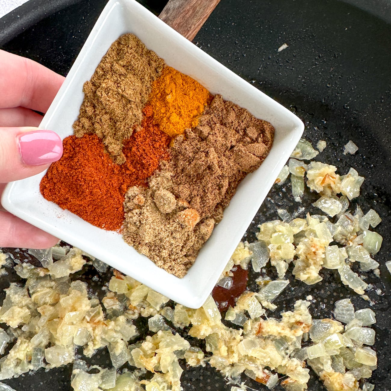 adding the spices to butter chicken onion