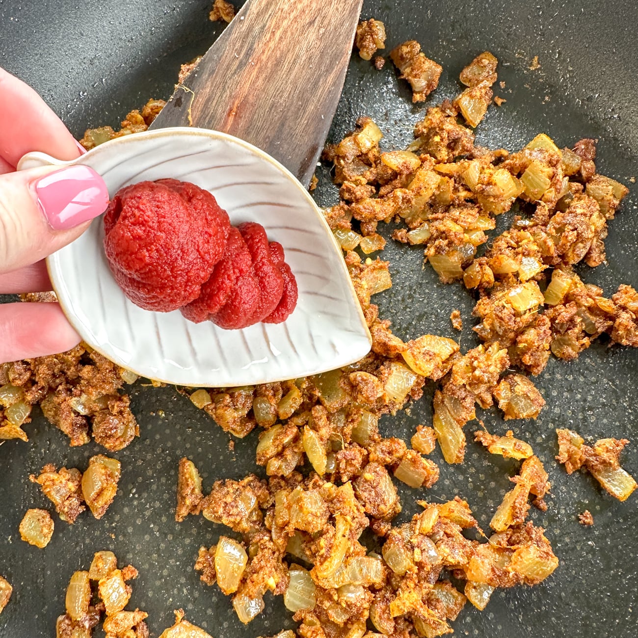 adding tomato paste to spiced onions