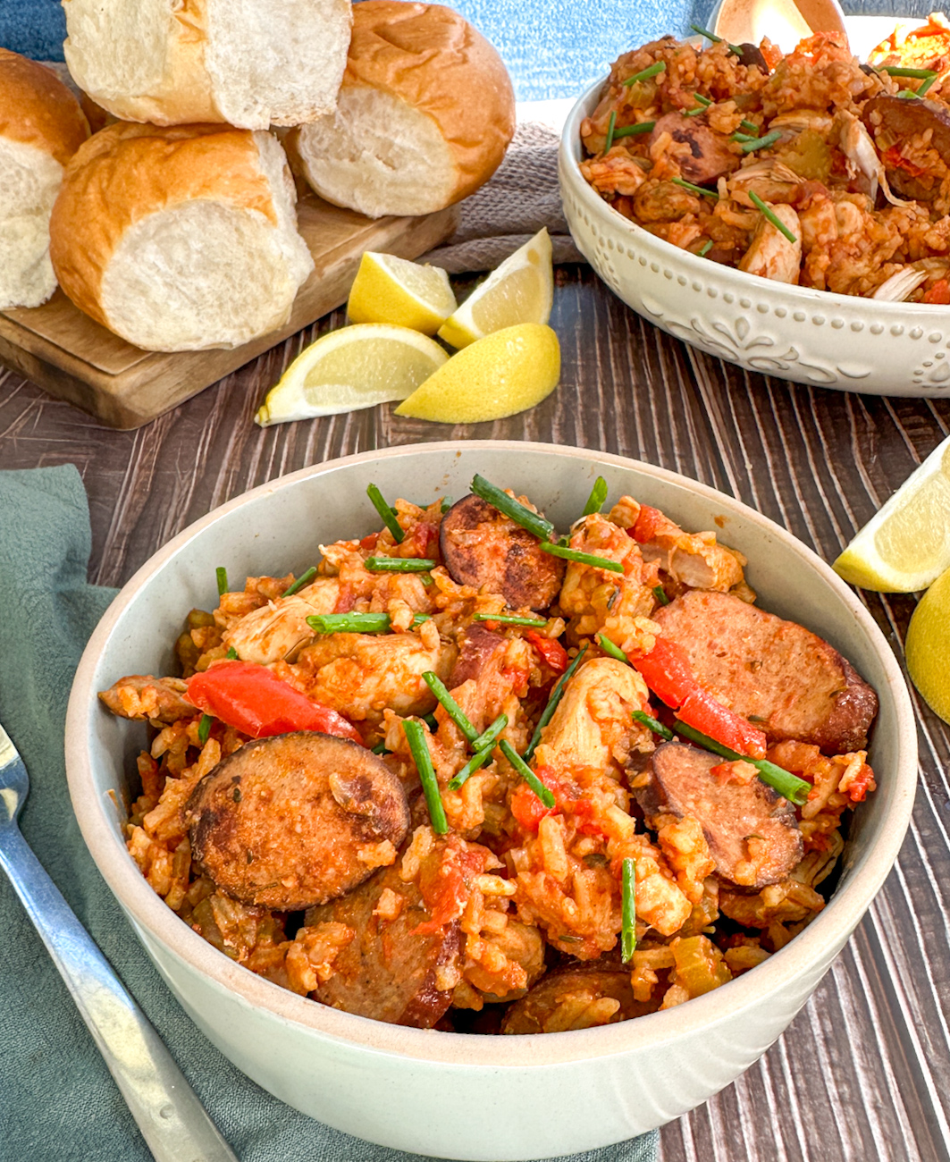 bowl of chicken and sausage jambalaya with rolls and lemon wedges