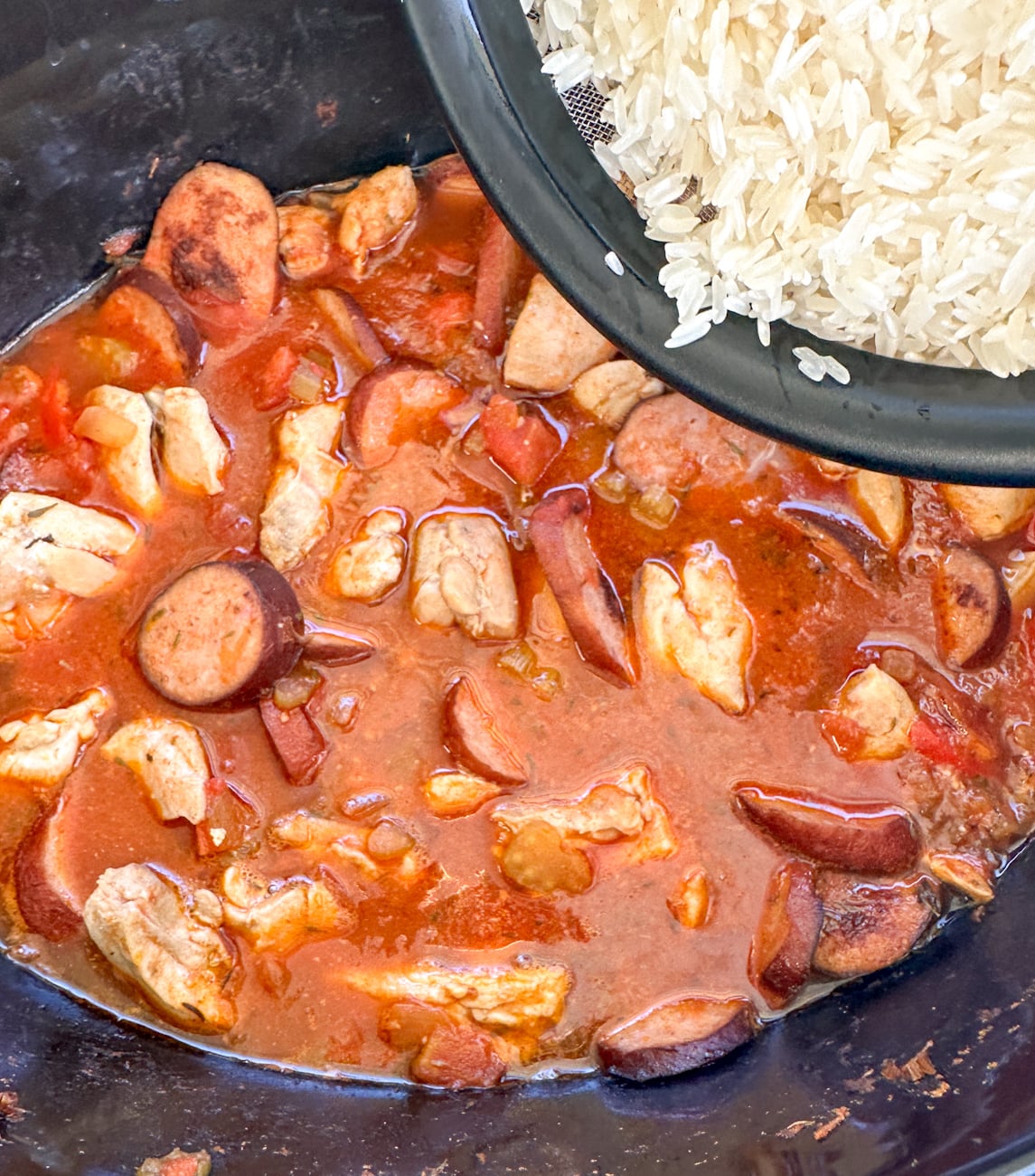 adding the rinsed rice to the slow cooker chicken and sausage jambalaya