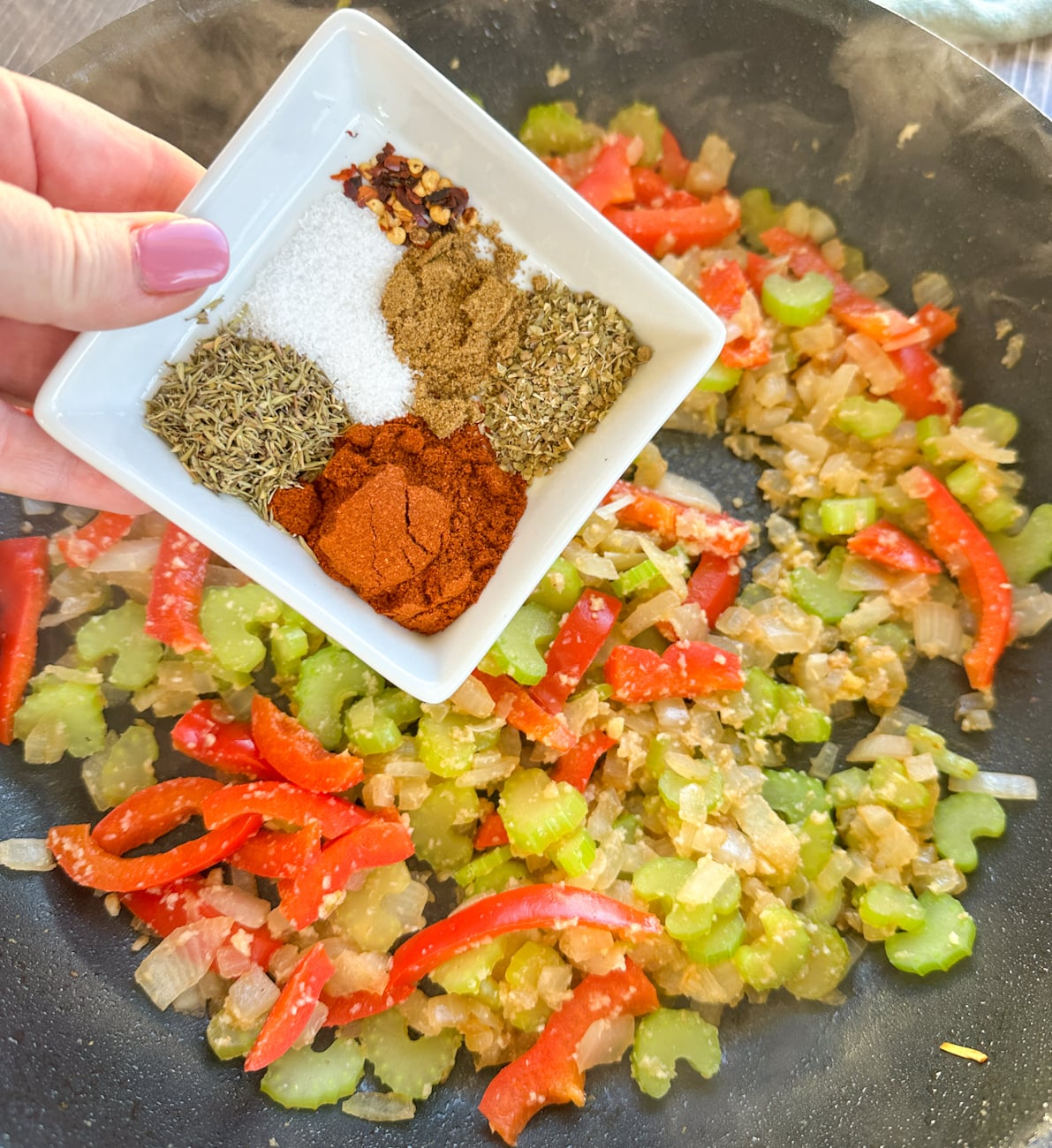 adding herbs and spices to the onion, bell pepper and celery for a jambalaya