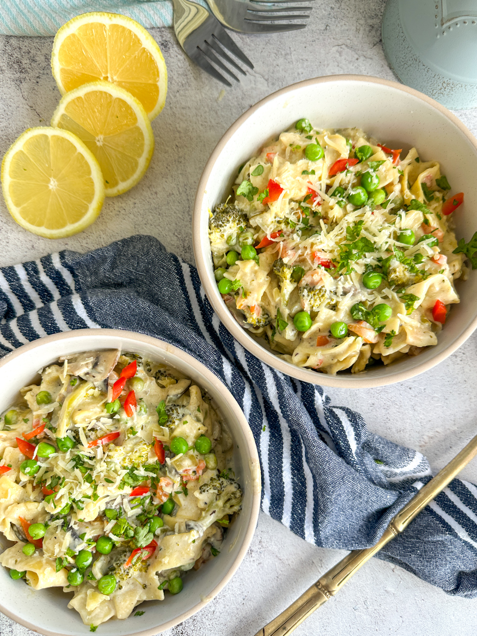 Two bowls of vegetarian creamy alfredo with garnish of parsley and lemon slices