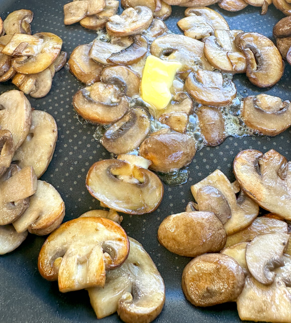 sauteeing mushrooms in a frying pan with butter