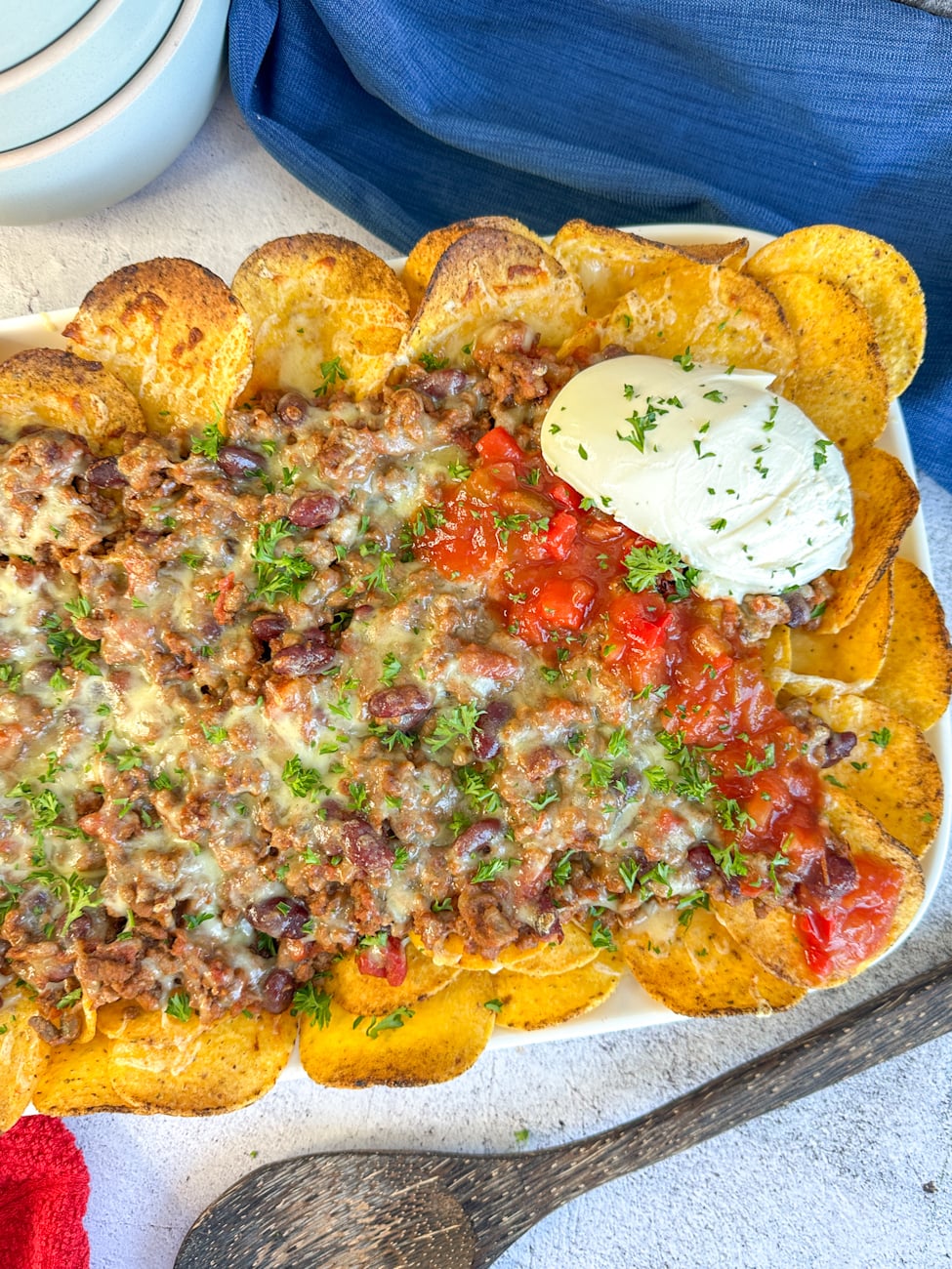 finished beef nacho chilli served over corn chips, with melted cheese sour cream and salsa