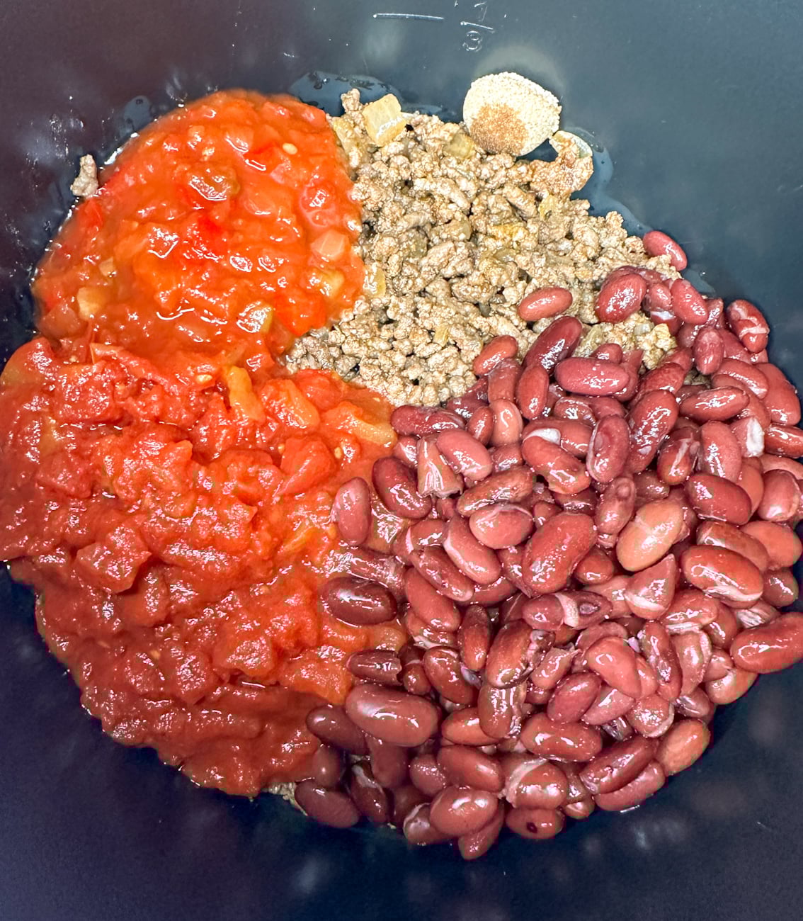 adding all ingredients for the beef chilli nachos into the slow cooker to cook