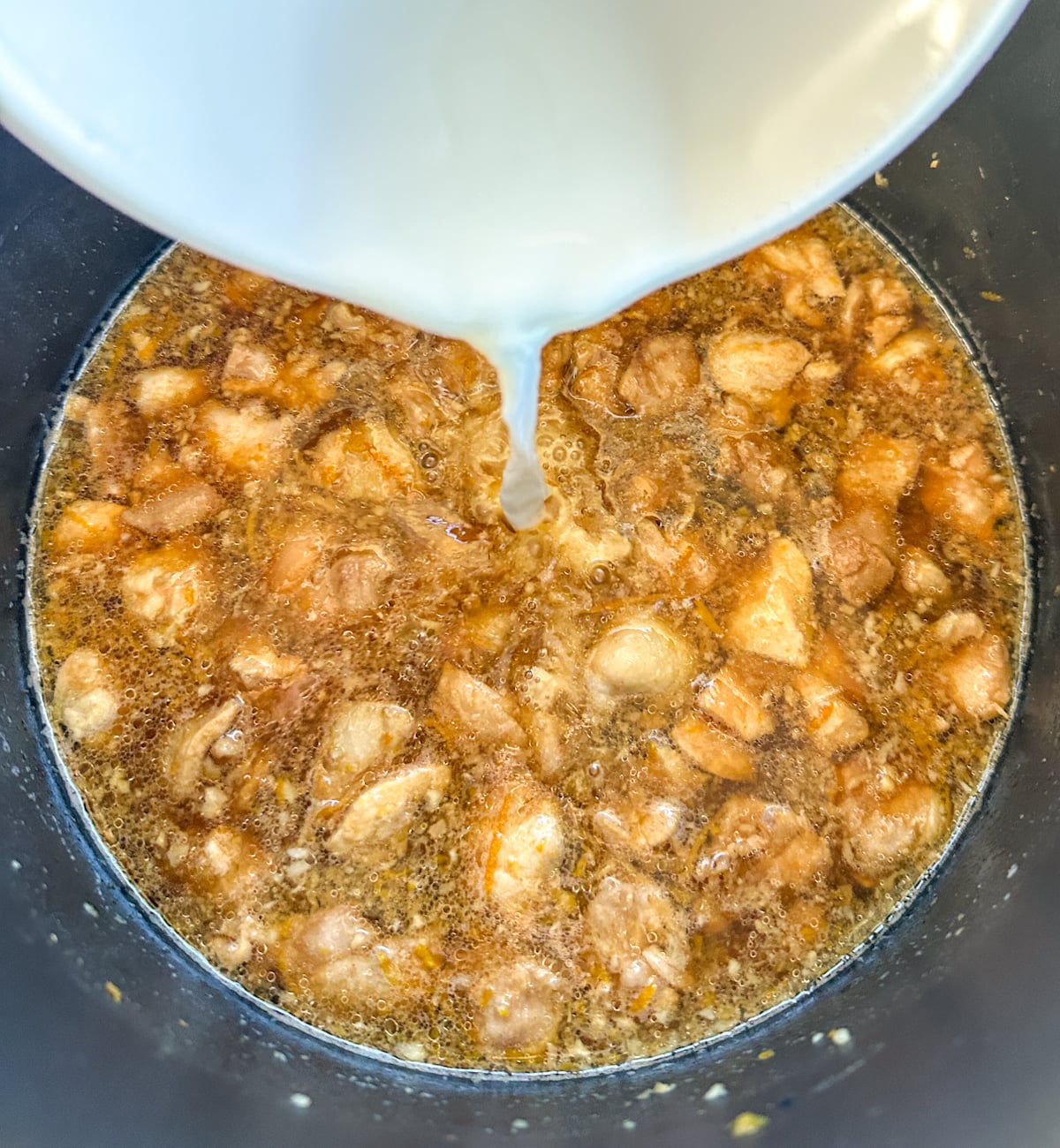 pouring a cornflour slurry into the cooked orange chicken to thicken