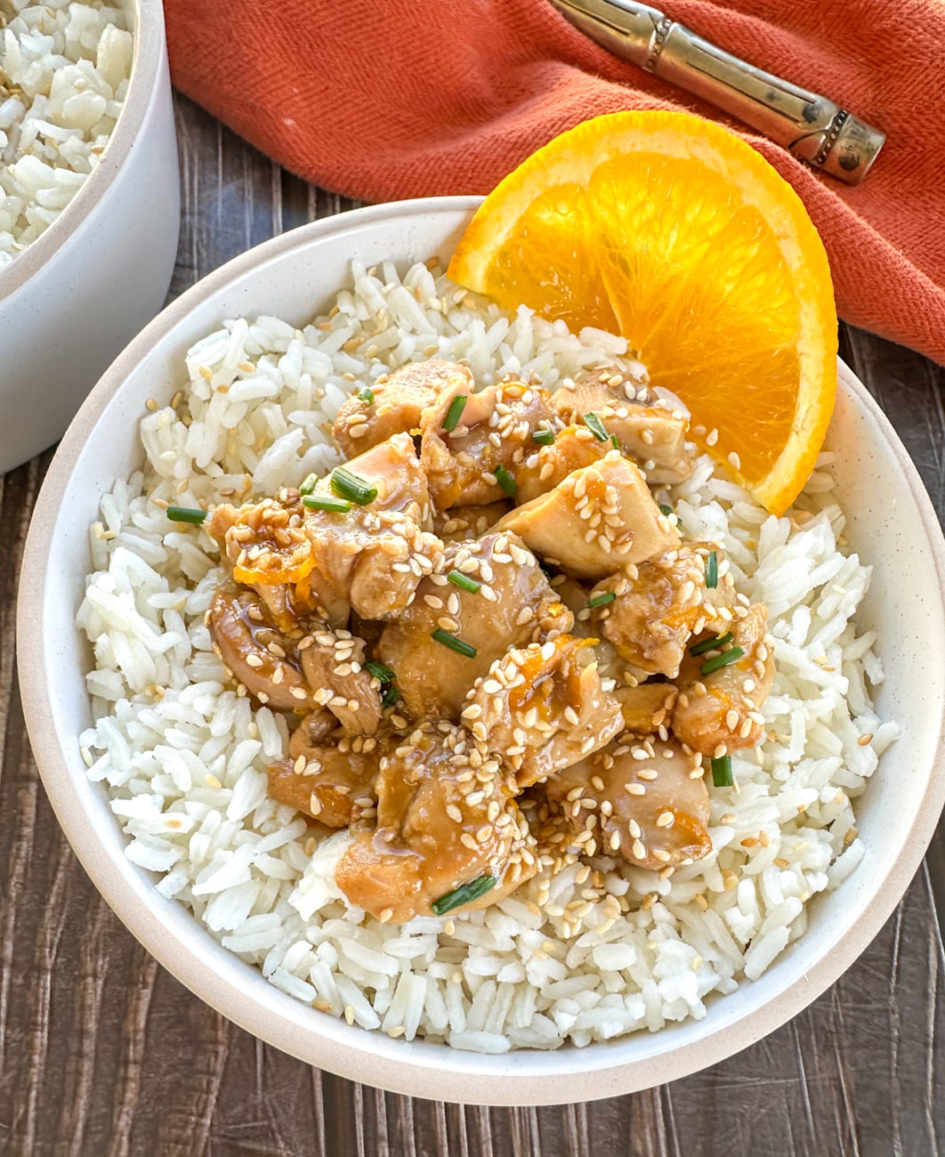 bowl of rice topped with orange chicken and a fresh slice of orange