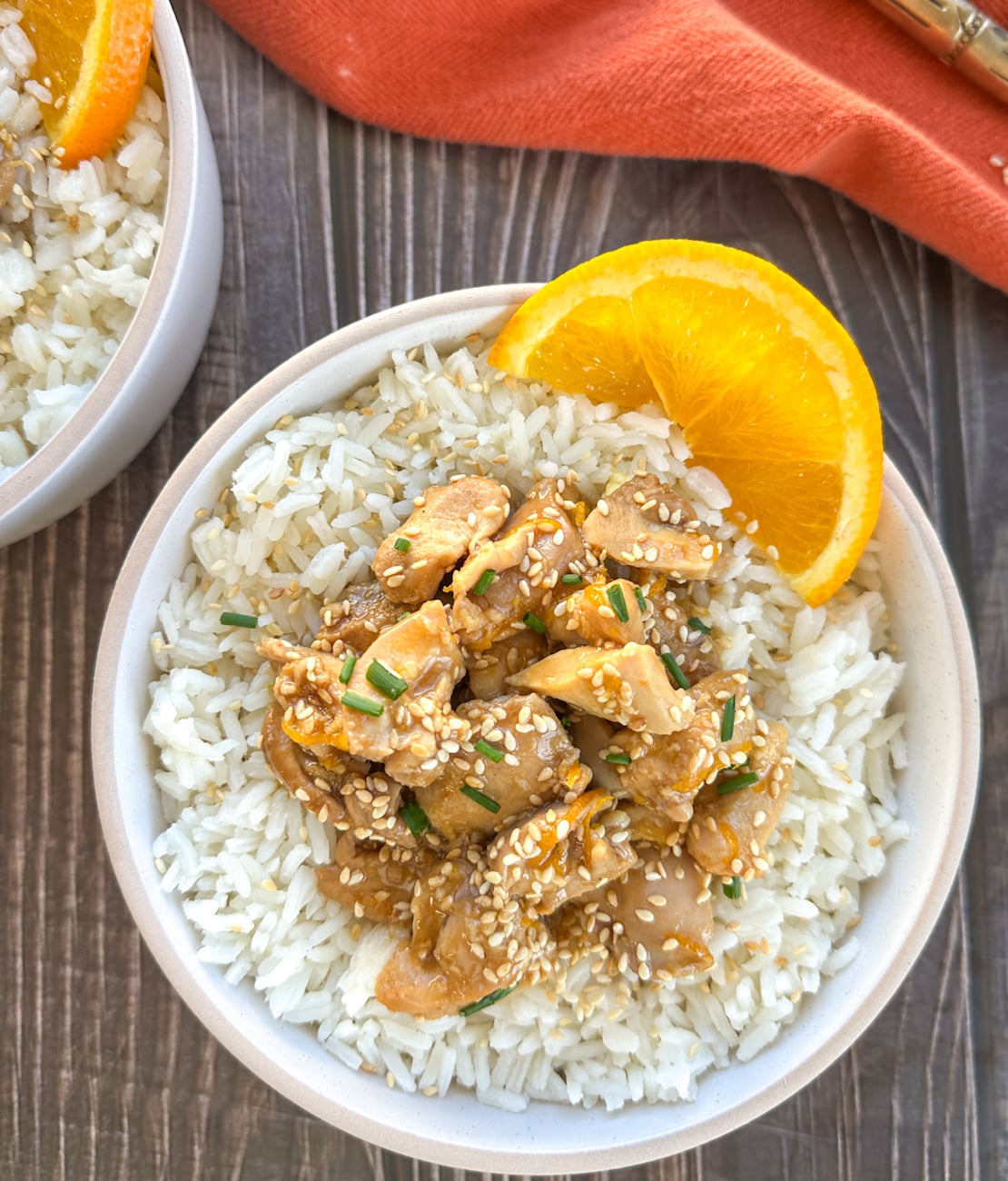 bowl of orange chicken served with rice and a fresh slice of orange