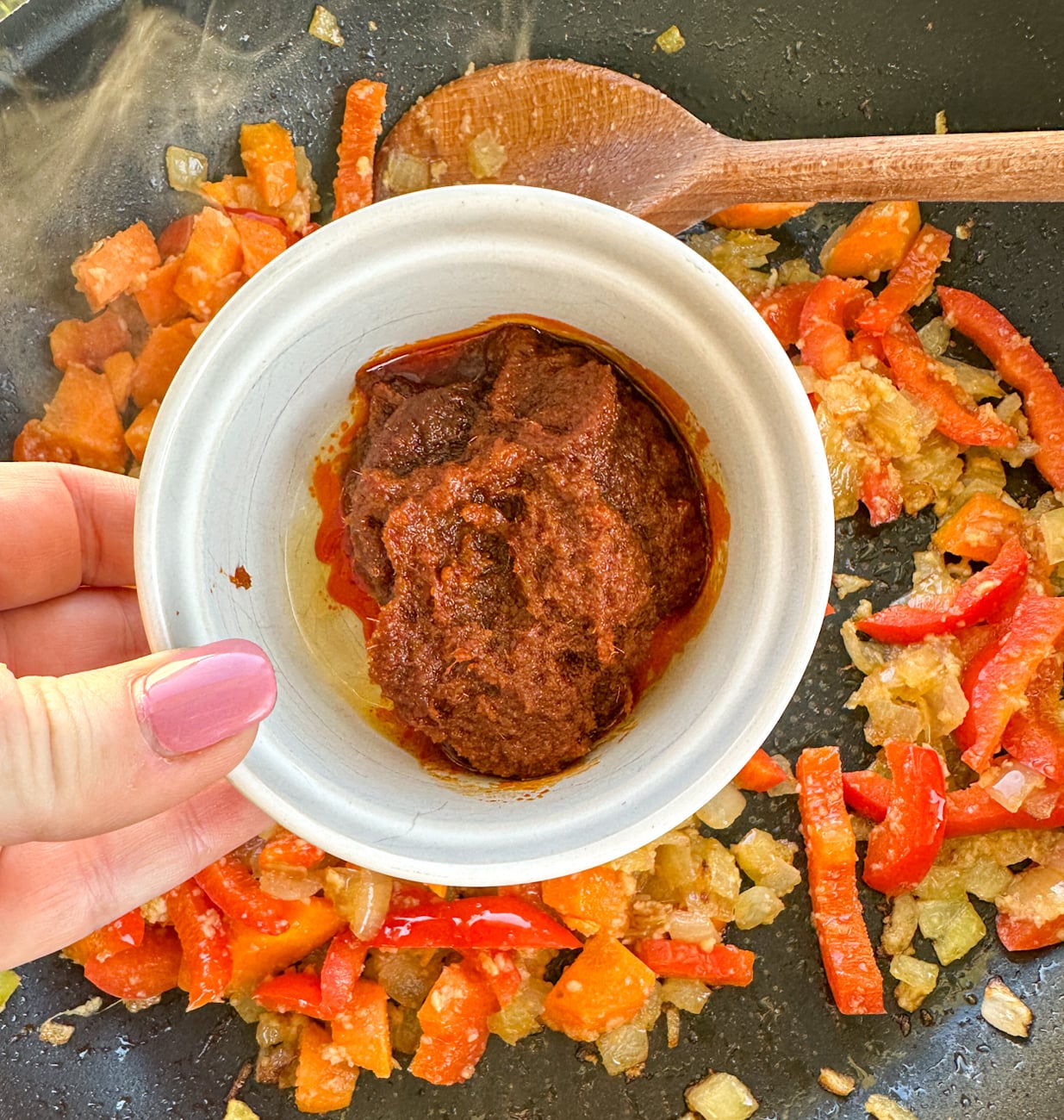 adding red thai curry paste into the sauted vegetables to fry off raw curry
