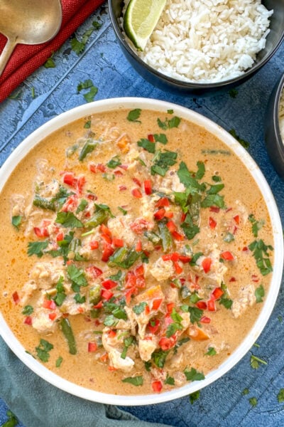 serving dish with a red thai chicken curry and rice bowls with lime wedges