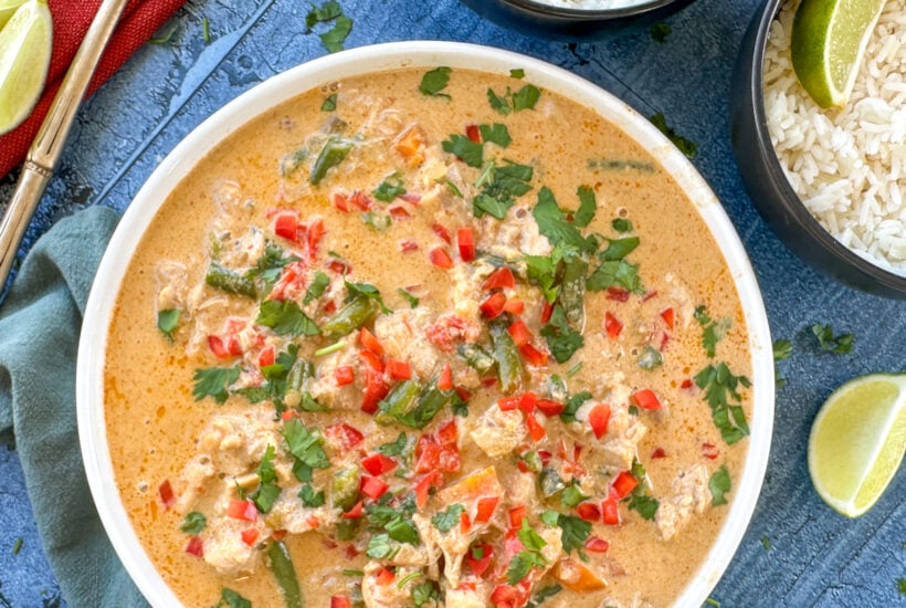 serving dish with a red thai chicken curry and rice bowls with lime wedges