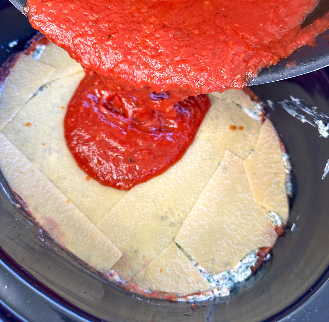 pouring sauce over the spinach and ricotta lasagna
