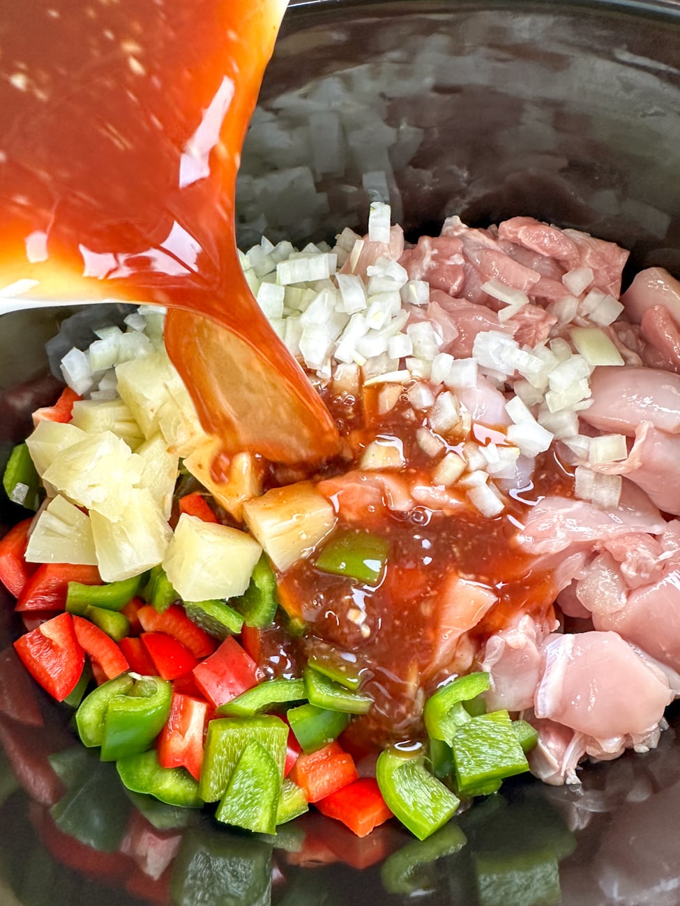 Adding the ingredients into the slow cooker for sweet and sour chicken and pouring over the sauce