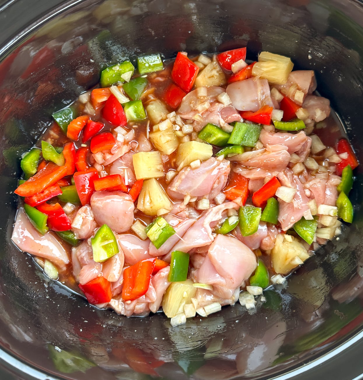 slow cooker full of ingredients ready to cook for sweet and sour chicken