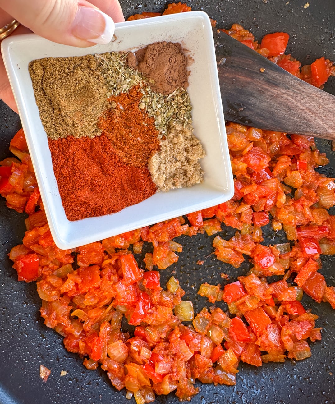 adding spices to the base of onions and red bell peppers