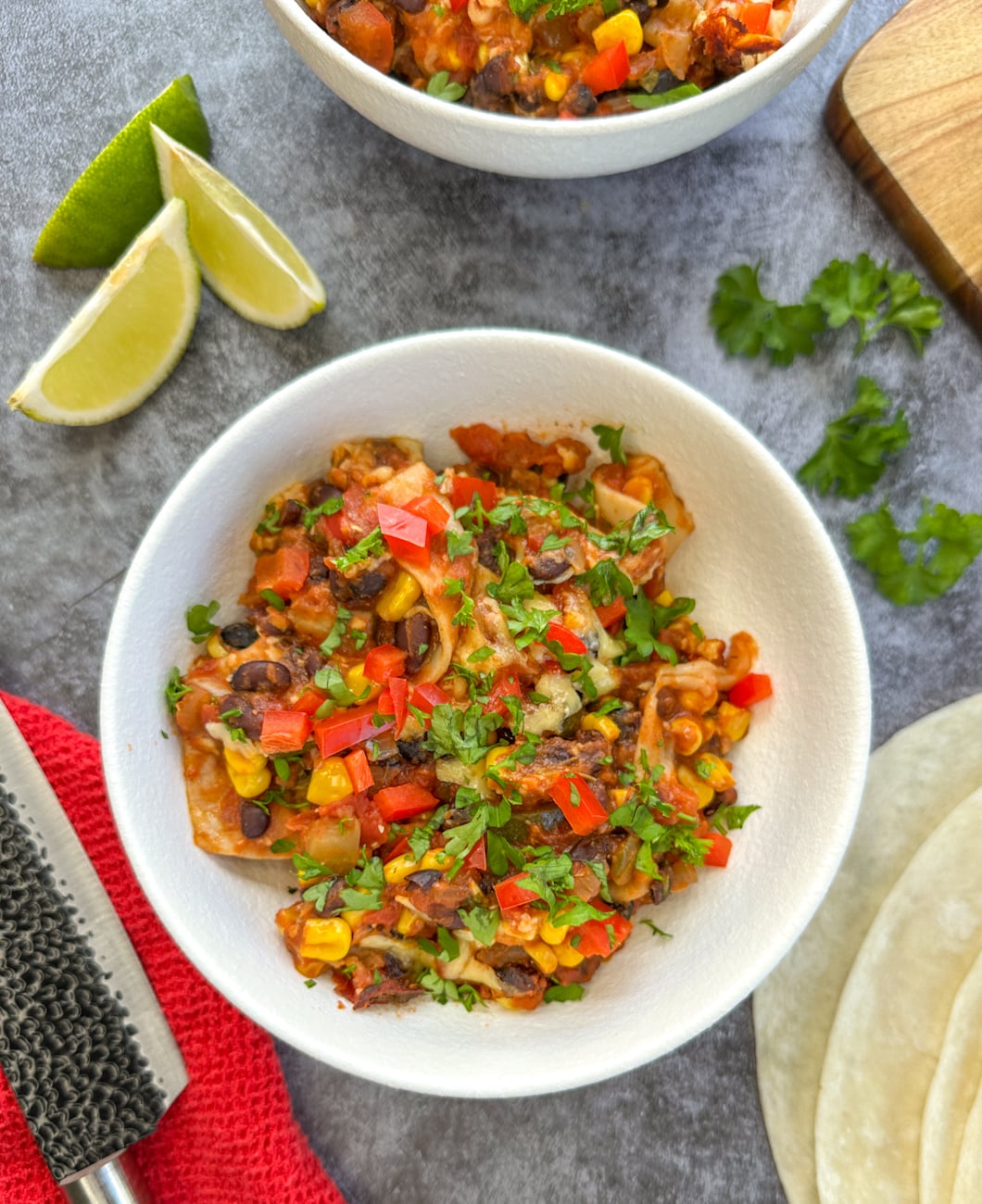 serving bowl with vegetarian enchilada casserole, lime wedges and coriander