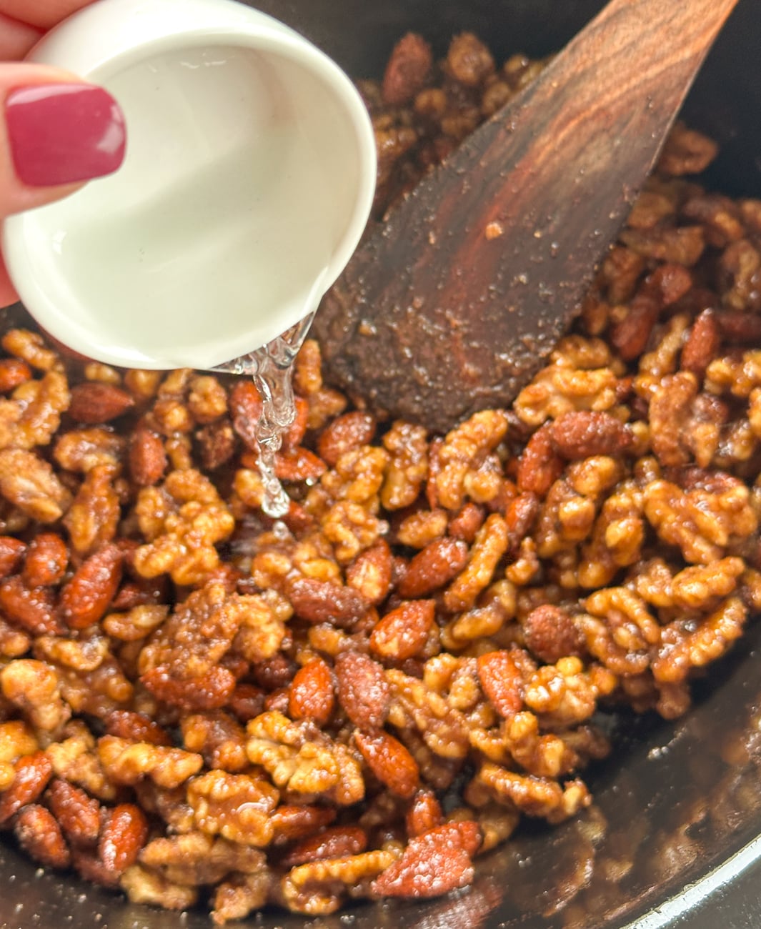 pouring water into the candied nuts in the slow cooker